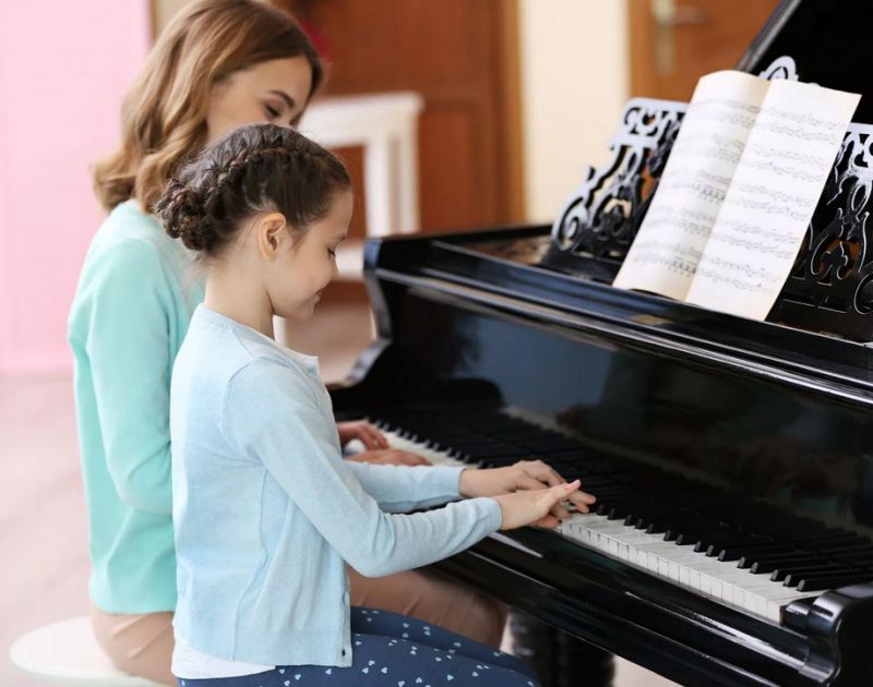 Девочка играет на пианино в присутствии учителя